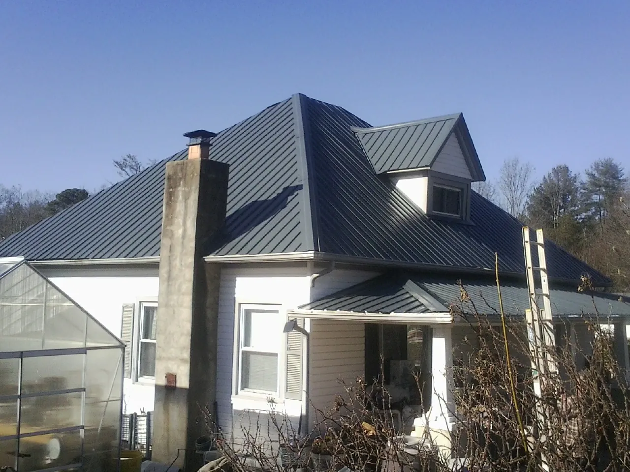 Dark blue standing seam metal roof on a white farmhouse with dormer — Slate & Tile Roof Repair by Roofing Brothers in Walled Lake