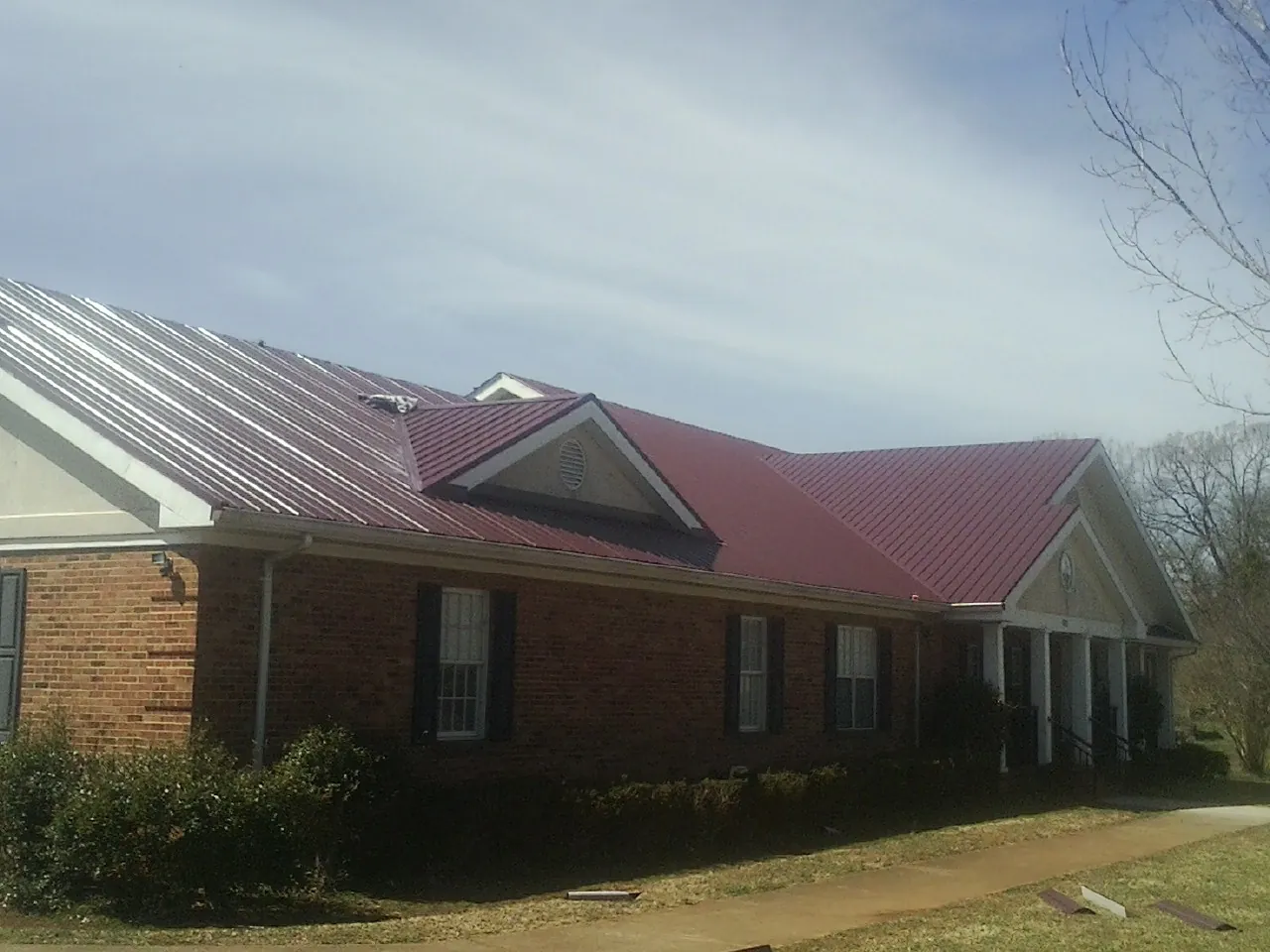 Red metal roof with gabled entries on a long brick building, from a Hail Damage Roof Repair job in Walled Lake