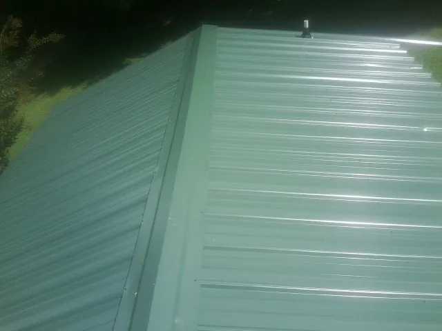 New green metal panels meeting at the ridge of a roof — Flat Roof Repair work by our crew in Walled Lake