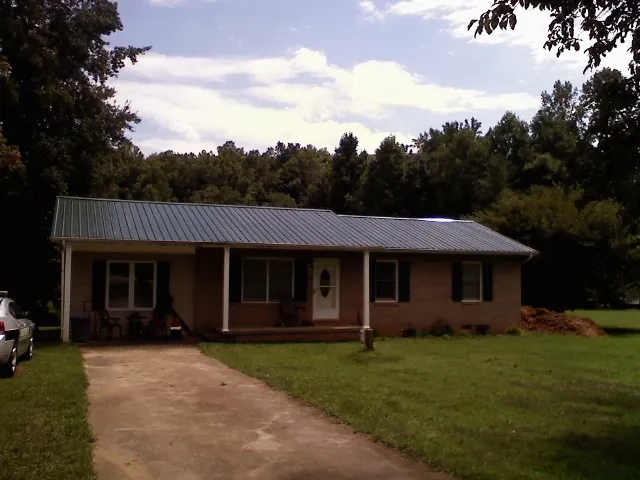 Dark green metal roof on a brick ranch with a covered porch in Walled Lake