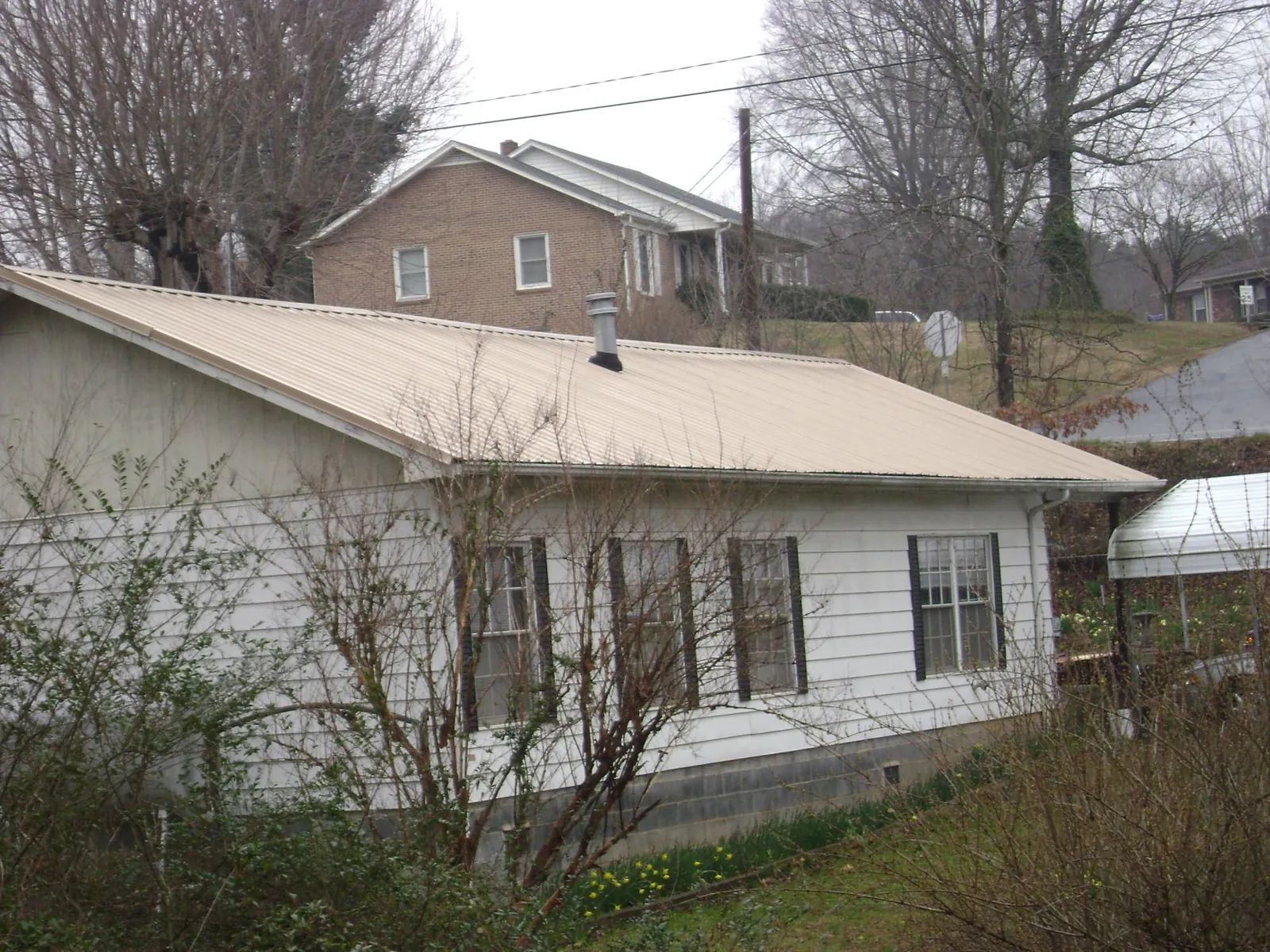 Tan metal roof on a white sided house set into a hillside — Commercial Roofing by Roofing Brothers in Walled Lake