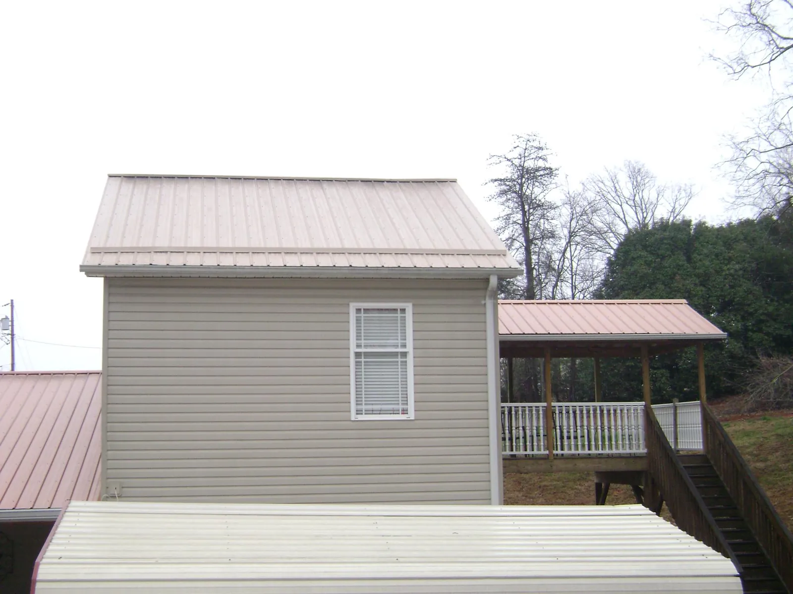 Tan metal roofs on a two story addition and attached porch, from a Roof Replacement job in Walled Lake